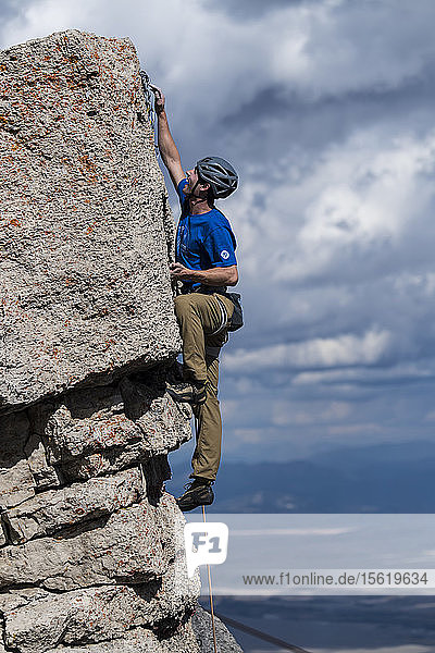 Male climber clipping rope to final anchor after reaching summit of rock  Jackson Hole  Wyoming  USA