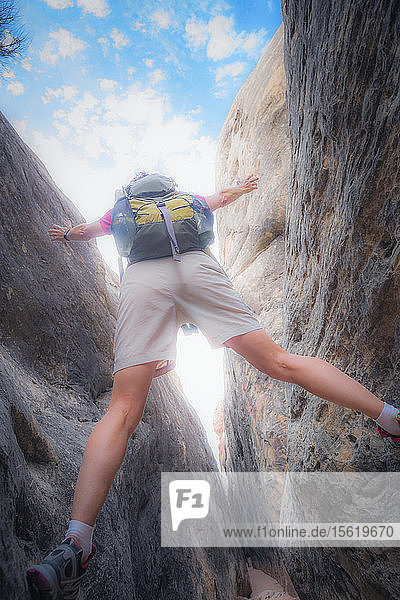 Blick von hinten auf eine Wanderin  die oberhalb eines Weges durch einen engen Slot Canyon im Canyonlands National Park  Utah  steht.