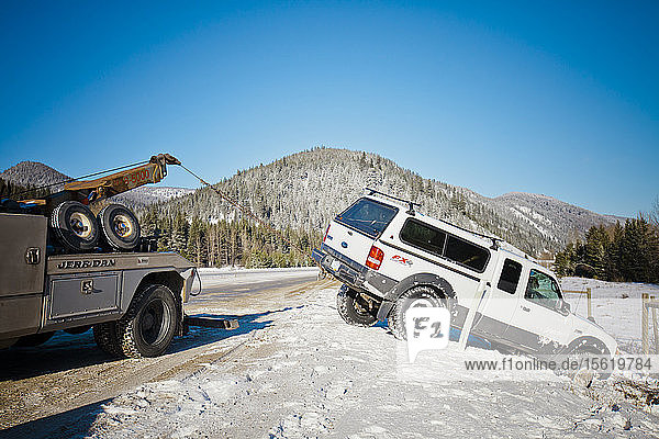 A tow truck pulls a mid-size truck out of a snow filled ditch on the side of the Coquihalla Highway  British Columbia  Canada.