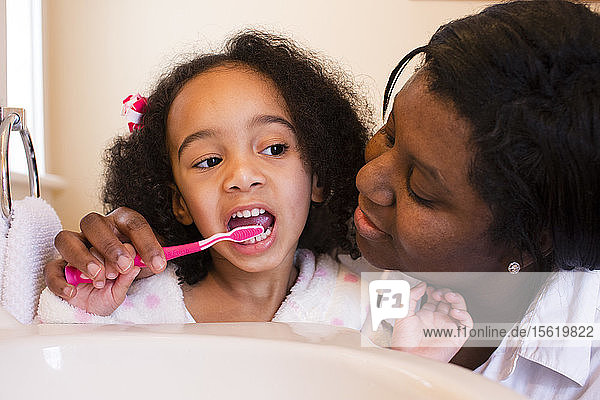 Eine Mutter hilft ihrer kleinen Tochter beim Zähneputzen.