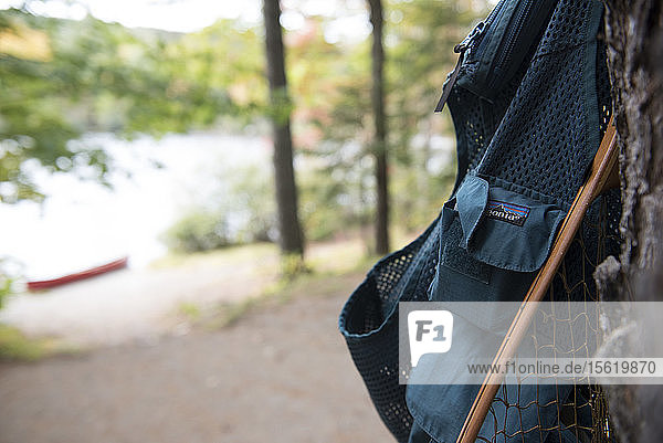 A Fly Fishing Vest And Net Hanging On A Tree Along A River In Maine