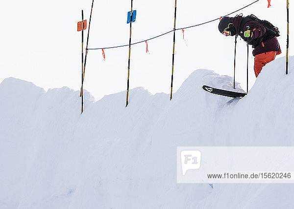 Ein Skifahrer duckt sich unter einem Seil hindurch und blickt auf seine bevorstehende Fahrt hinunter.
