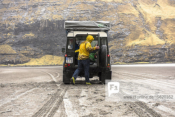Rückansicht eines Mannes  der in den Kofferraum eines Geländewagens in natürlicher Umgebung schaut  Färöer Inseln  Dänemark