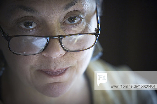 Porträt einer Frau mittleren Alters  die über eine Brille hinweg in die Kamera starrt.