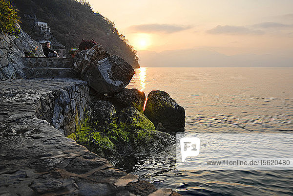 Steinweg am Ufer des Atitl?ï¿½n-Sees  Guatemala  mit einer Frau  die den Sonnenaufgang beobachtet