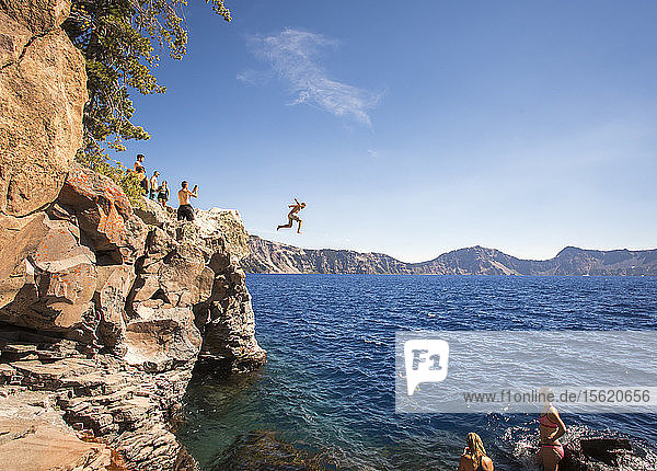 Young people wait on a rock outcrop and swim or jump into the deep blue waters of a mountain lake  Crater Lake  Oregon  USA