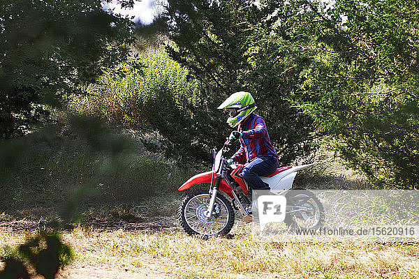Side view shot of a single boy riding a motorcycle in a forest