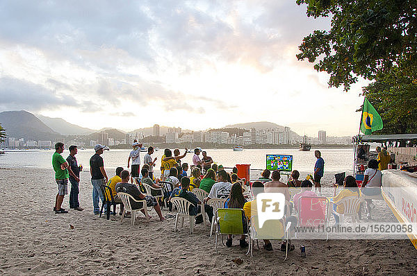 Eine Gruppe lokaler Fußballfans schaut sich am Strand ein Fußballspiel im Fernsehen an
