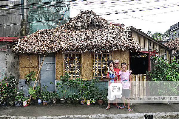 Porträt von Großeltern mit Kind  die vor einer Strohhütte in die Kamera schauen  Legazpi City  Provinz Albay  Philippinen