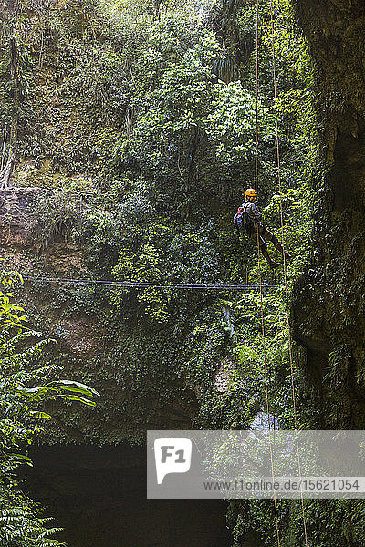 A Woman Rappels Into A Deep Cave In A Lush Forest In Puerto Rico
