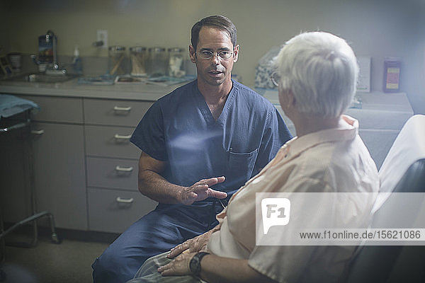 A physician discuss a point with his patient who sits in front of him.