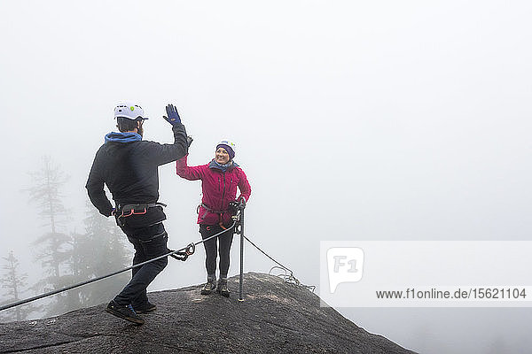 A man and a women slap a hi-five while doing the Via Ferrata on a rainy fall day in Squamish  British Columbia.