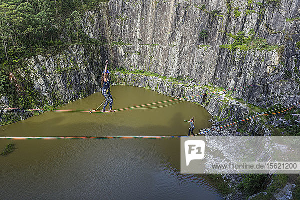 Adventurous man and woman crossing quarry in opposite directions on separate slacklines Dibs Quarry Maripora Sao Paulo State Brazil