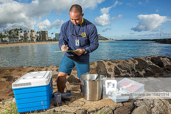 Wataru Kumagai von der Abteilung für sauberes Wasser des Gesundheitsministeriums des Bundesstaates Hawaii demonstriert am Ala Moana Beach in Honolulu die Entnahme von Wasserproben an hawaiianischen Stränden mit Instrumenten wie einem Trübungsmessgerät. Um den vollen Umfang der Messwerte zu erhalten  müssen die Laborarbeiten außerhalb des Landes durchgeführt werden.