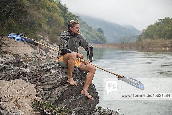 Jan aus den Niederlanden posiert mit seinem Bambus- und Flossenpaddel auf diesem Campingplatz am Ufer des Nam Ou Flusses in Laos. Er paddelte schließlich von Muang Khua nach Nong Khiaw auf einem Bambusfloß  das er mit Hilfe von Einheimischen gebaut hatte.