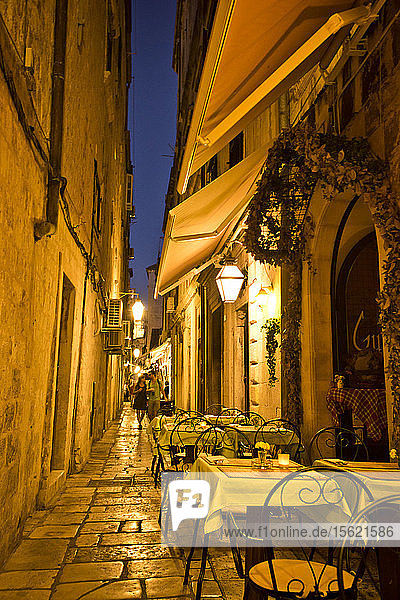 In der Abenddämmerung werden in einer Gasse in Dubrovnik  Kroatien  Restauranttische beleuchtet.