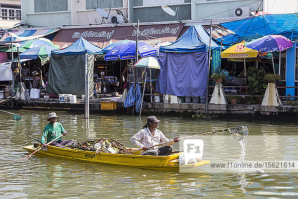 Zwei Männer auf einem Boot entfernen Müll aus dem Wasser auf dem schwimmenden Markt von Amphawa  Thailand