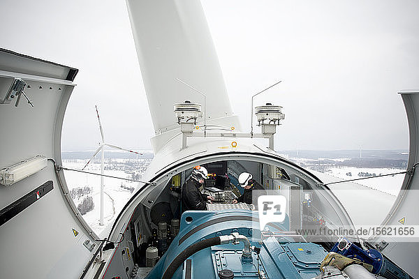 Zwei Wartungsarbeiter arbeiten im Winter an einer Windkraftanlage in Nordpolen bei Kobylnica: Dieses Foto von Experten bei der Arbeit zeigt eine ungewöhnliche Perspektive auf Windturbinen und wird wahrscheinlich als glaubwürdig und authentisch angesehen