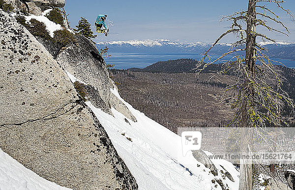 Snowboarder jumping off rock and over Lake Tahoe
