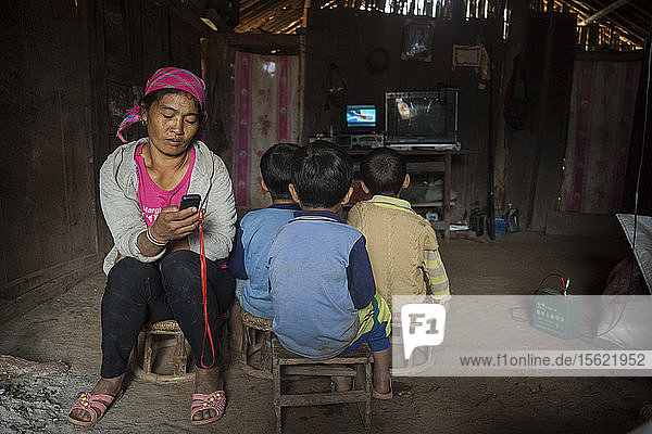 Eine Mutter spielt Musik von ihrem Handy ab  während ihr Sohn und zwei seiner Freunde zu Hause in Ban Sop Kha  Laos  fernsehen. Die elektronischen Geräte werden mit Batterien (rechts) betrieben  die von Kleinstwasserturbinen geladen werden  die in den Nam Ou-Fluss eingebaut wurden.