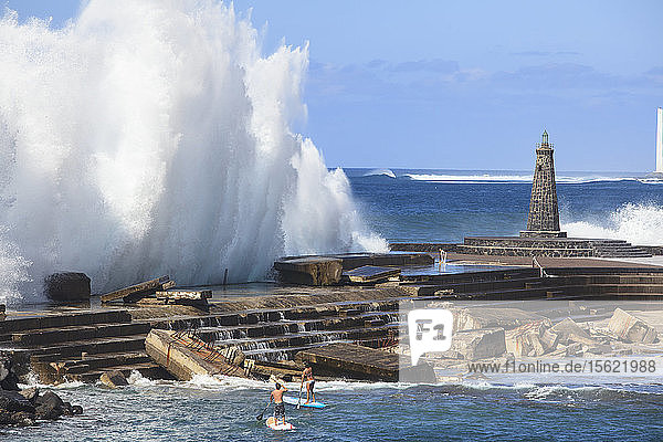 Die Profi-SUP-Athleten Iballa Ruano und Vilayta beobachten die Wellen  die sich an einem Pier auf den Kanarischen Inseln brechen.