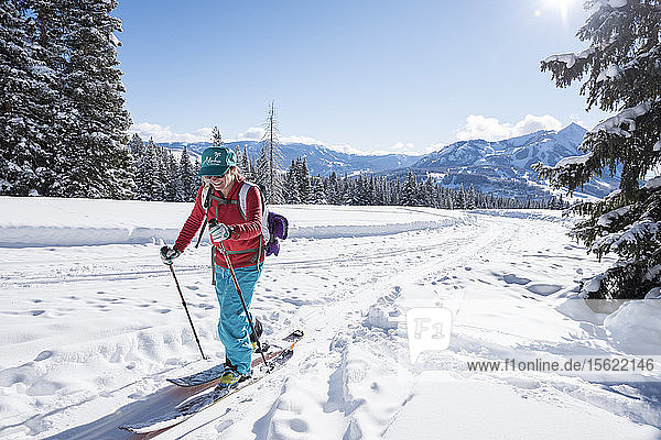 A skier with an Aloha hat on makes her way onto the skin track from an old road with Mt Crested Butte behind her.