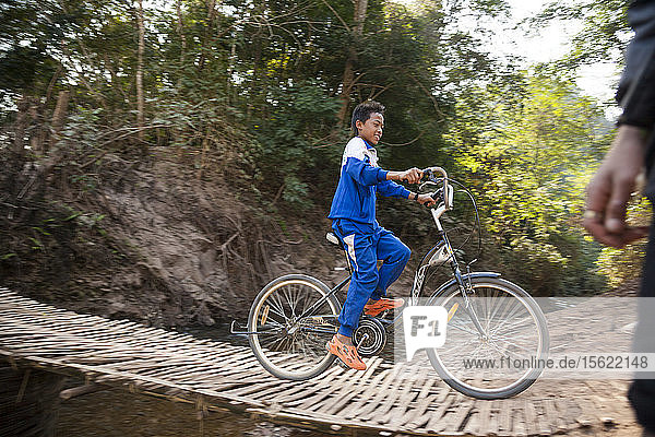 A boy rides his bicycle over the woven bamboo bridge over the tributary stream to the Nam Ou River outside Ban Huay Phouk  Laos.