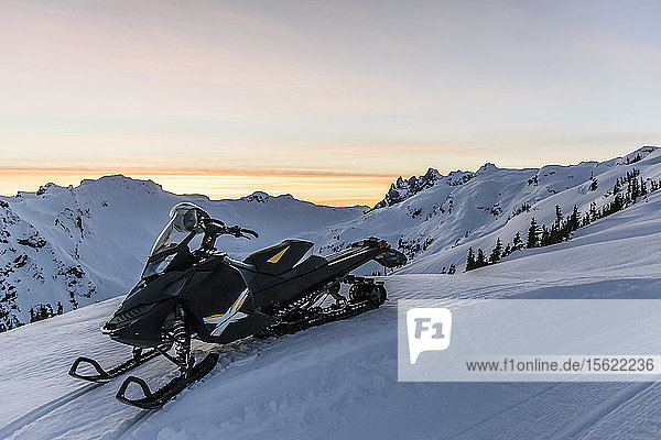 Einzelnes Schneemobil auf einem Berg im Winter unter stimmungsvollem Himmel bei Sonnenuntergang  Callaghan Valley  Whistler  British Columbia  Kanada