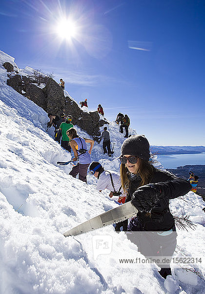 Professioneller Skifahrer schneidet mit einer Schneesäge einen Block  um eine Sprungschanze zu bauen