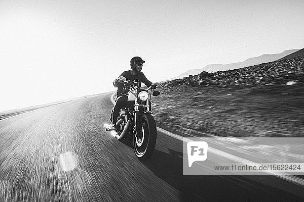Ein Mann fährt mit seinem Harley Davidson-Motorrad auf einer leeren Straße in der Wüste kurz vor Sonnenuntergang
