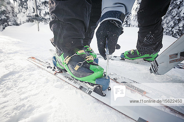 Skifahrer mit Schraubenzieher zum Einstellen der Din-Einstellung an der Bindung seines Partners