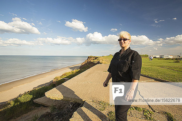 Woman stands next to the edge of collapsing coastal cliffs at Aldbrough on Yorkshires East Coast  UK. She is stood in the location where her house used to be  before being evacuated  as the house was dangerously close to the edge. The coast is composed of soft boulder clays  very vulnerable to coastal erosion. This section of coast has been eroding since Roman times  with many villages having disappeared into the sea  and is the fastest eroding coast in Europe. Climate change is speeding up the erosion  with sea level rise  increased stormy weather and increased heavy rainfall events  all playing their part.