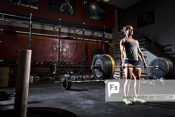 Ein sportliches Mädchen trainiert mit schweren Gewichten an einer Langhantel in einem düsteren Fitnessstudio in San Diego  Kalifornien.