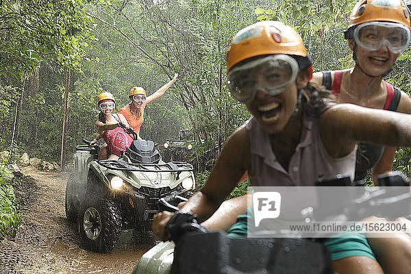 Women laughing while driving quad bikes in Emotions Native Park during rain  Quintana Roo  Mexico