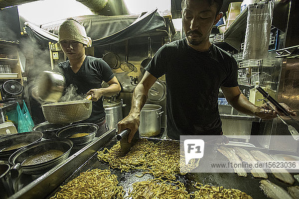 Frontansicht von zwei Arbeitern  die in einem Ramen-Laden kochen  wobei einer die Nudeln schneidet und brät  Tokio  Japan