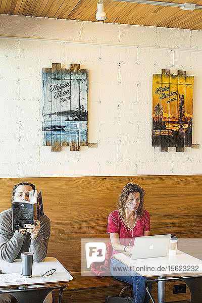 Man reading book sitting at cafe next to woman typing on laptop  Seattle  Washington  USA