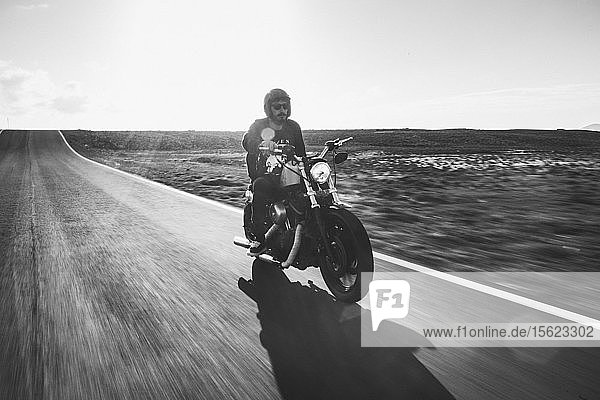 Ein Mann fährt mit seinem Harley Davidson-Motorrad auf einer leeren Straße in der Wüste kurz vor Sonnenuntergang