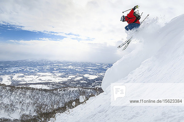 A male skier is jumping in the air onto a slope with deep powder snow in the ski resort Niseko United on the Japanese island of Hokkaido.
