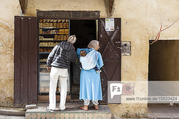 Marokkanischer Mann mit einer marokkanischen Frau in traditioneller Kleidung (Djellaba) mit ihrem kleinen Sohn auf dem Rücken in einem kleinen Straßenladen in Fez  Marokko.