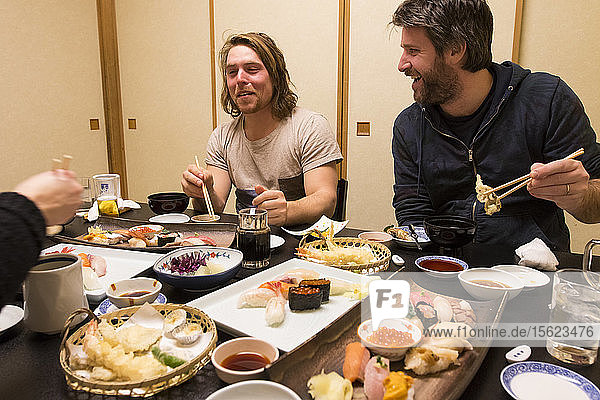 Ein europäischer Mann macht das Wasabi-Gesicht  während er in der Hafenstadt Otaru  Hokkaido Japan  Sushi isst  während seine Freunde lachen.