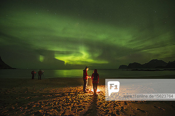 Ruhige Szene mit Menschen am Lagerfeuer am Strand unter Polarlicht  Flakstadoya  Lofoten  Norwegen  bei Nacht