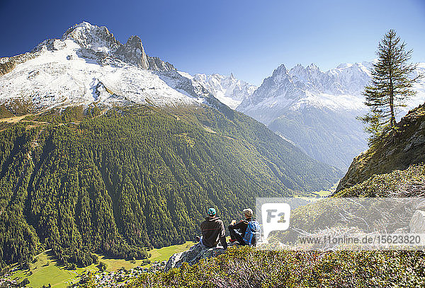 Two hikers are enjoying the view on the Mont Blanc mountains while taking a rest on the Tour du Mont Blanc. They are on their way to Lac Blanc  above the Chamonix valley.