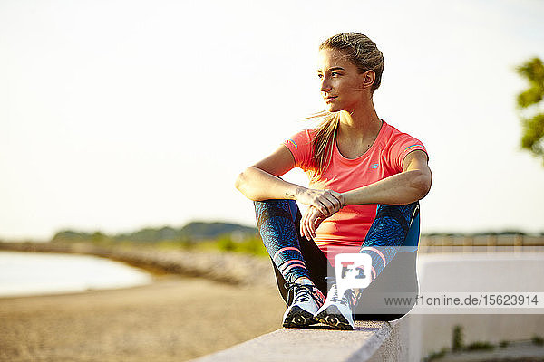 A Young Athletic Woman Sitting Of Wall Enjoying View Of Beach