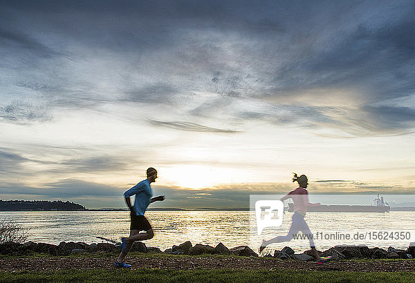 Side view of man and woman running along Puget Sound at sunset  Seattle  Washington State  USA