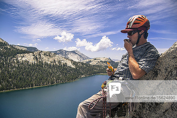 Blick auf einen einzelnen abenteuerlustigen Mann  der beim Klettern oberhalb eines Sees in Tuolumne Meadows  Yosemite National Park  Kalifornien  USA  einen Snack zu sich nimmt