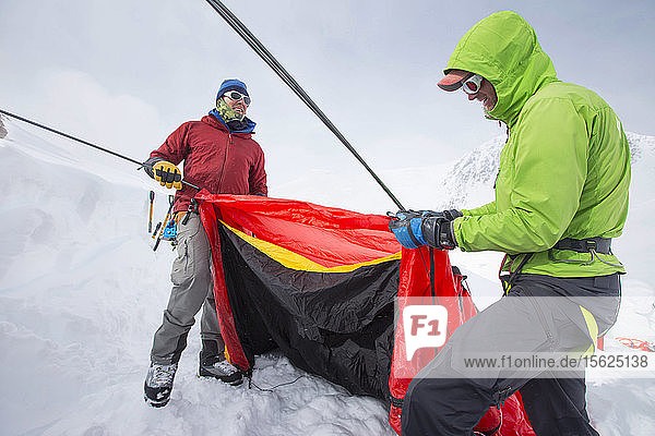 Zwei Bergsteiger bauen bei kaltem und stürmischem Wetter ein Zelt auf dem Denali auf