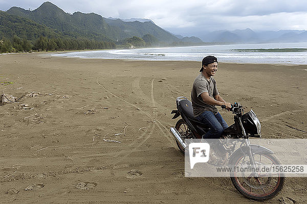 Cheerful smiling Asian man on motorcycle on beach  Banda Aceh  Sumatra  Indonesia