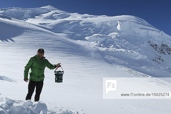A ranger holding a portable toilet known as Clean Mountain Can on Denali  Alaska. With the clean climbing policy Denali National Park tries to force mountaineers to keep the Alaska mountains clean. In early days contaminated water made many alpinists sick. Nowadays all human waste have to be put in biodegradable bags that are dumped into crevasses.