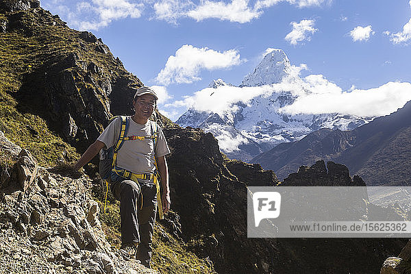 Sange Sherpa  ein nepalesischer Bergführer  steht für ein Foto entlang der Trekkingroute zum Everest-Basislager  in der Ferne ist die Ama Dablam zu sehen  die der Führer bereits bestiegen hat  Phortse  Solu Khumbu  Nepal