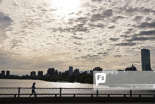 Silhouette einer Frau  die bei Sonnenuntergang auf einer Brücke am Charles River läuft  Boston  Massachusetts  USA